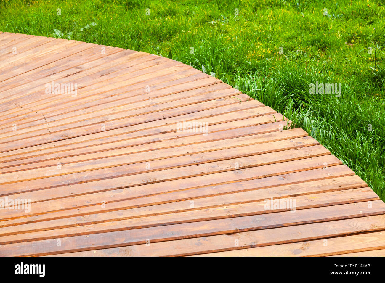 Turning new wooden boardwalk over lawn with green grass, modern park background Stock Photo