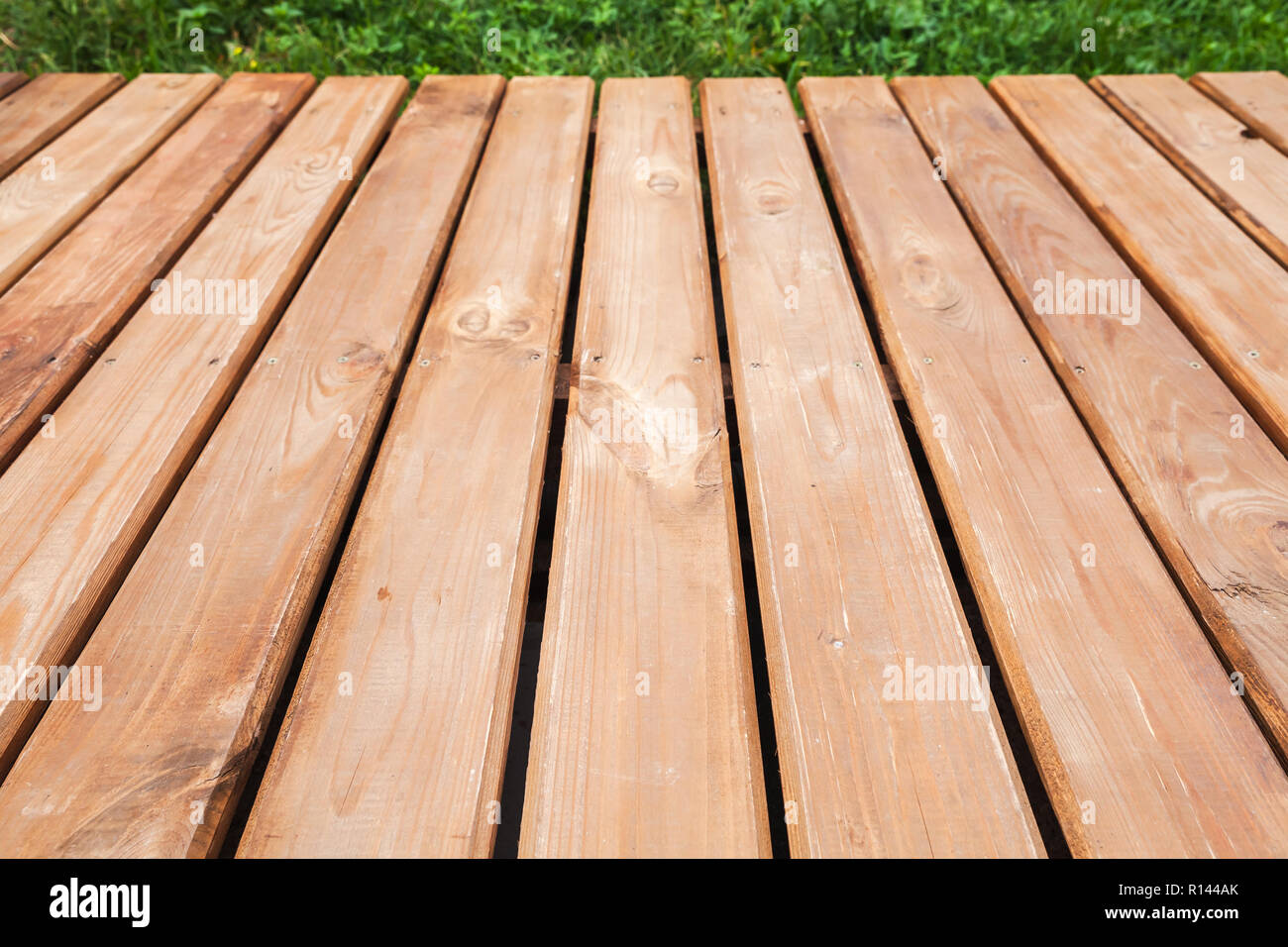 Perspective view of wooden boardwalk over lawn with green grass, modern park background. Close-up photo with selective focus Stock Photo