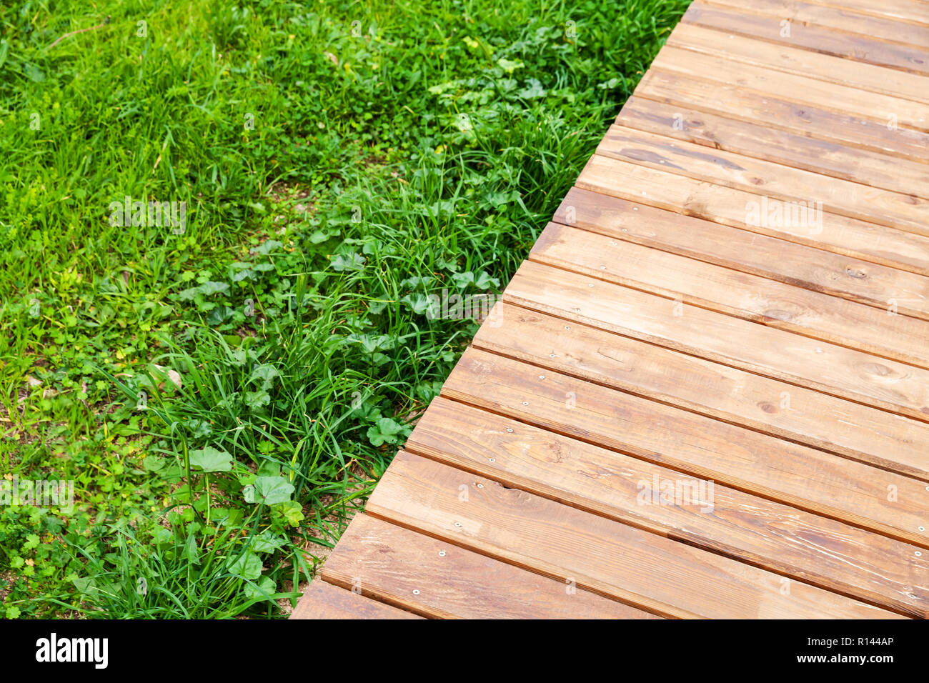 New wooden boardwalk over lawn with green grass, modern park background Stock Photo