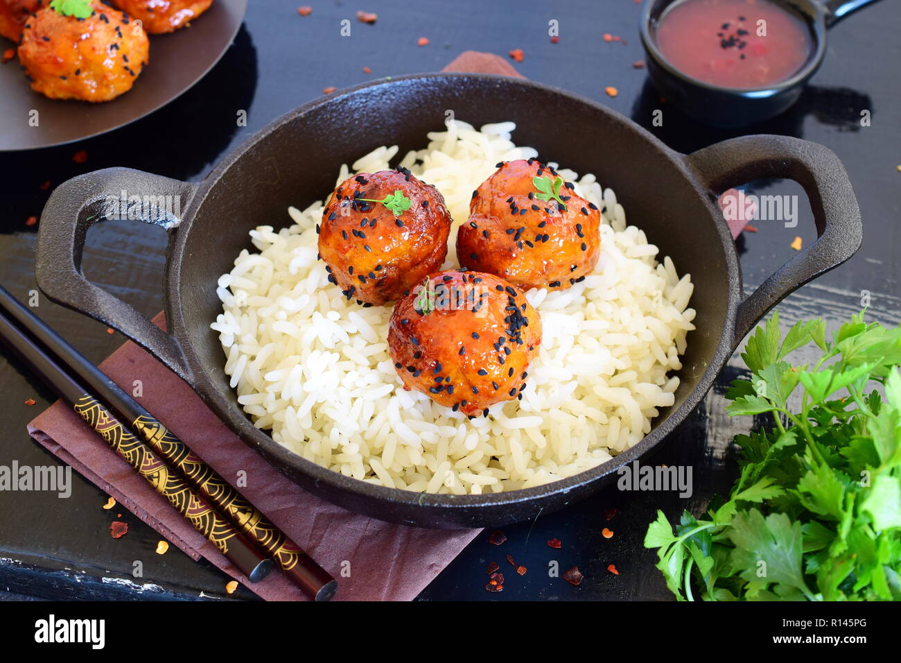 Spicy chicken balls in sweet chilly glazur with rice in a frying pan on a black wooden background Stock Photo
