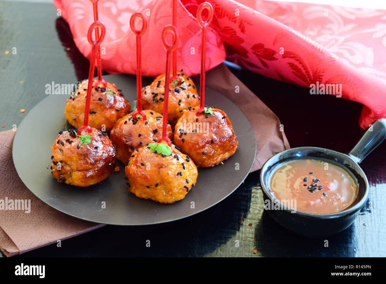 Spicy chicken balls in sweet chilly glazur on a metal tray on a black wooden background Stock Photo