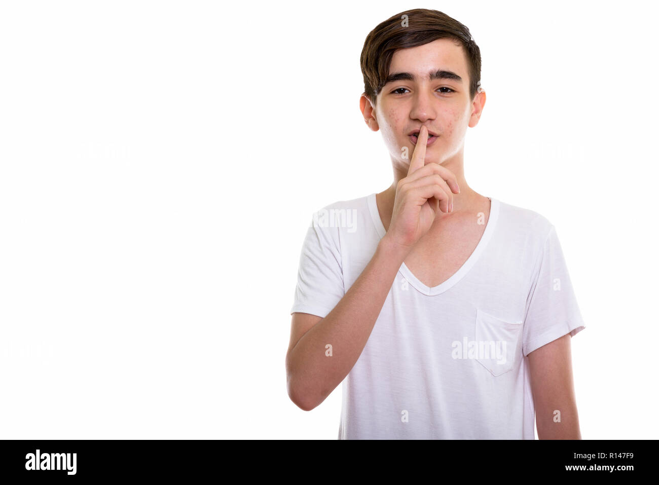 Studio shot of young handsome Persian teenage boy with finger on Stock Photo