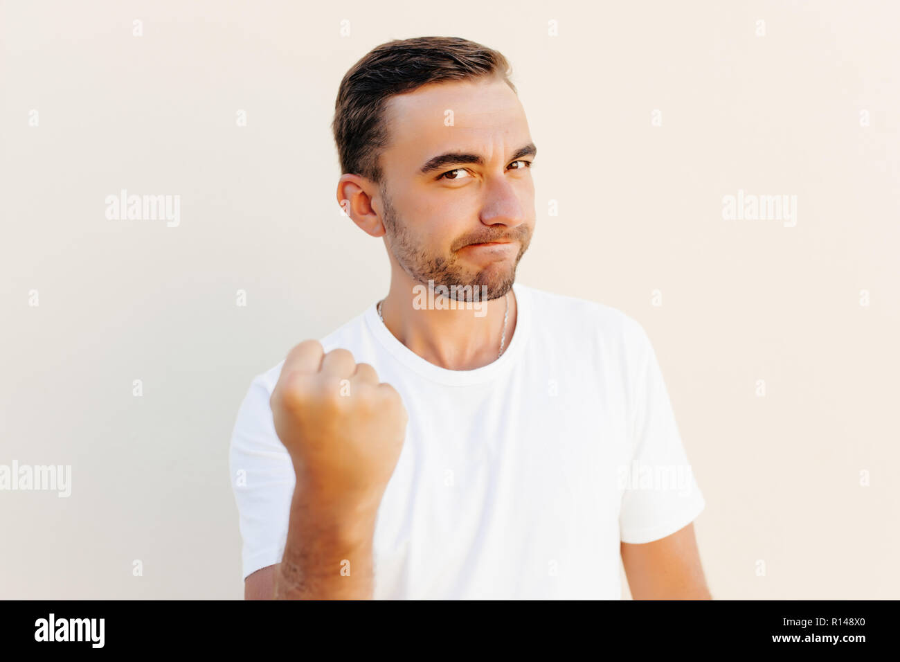 Closeup portrait, angry cranky upset young man, worker, business putting up fist about to give you knuckle sandwich, isolated orange background. Stock Photo