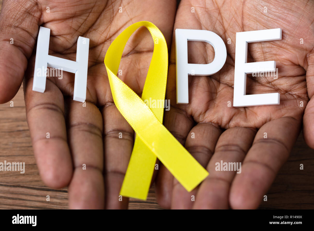 Person's Hand Holding Ribbon With Hope Text To Support Childhood And Bladder Cancer Stock Photo