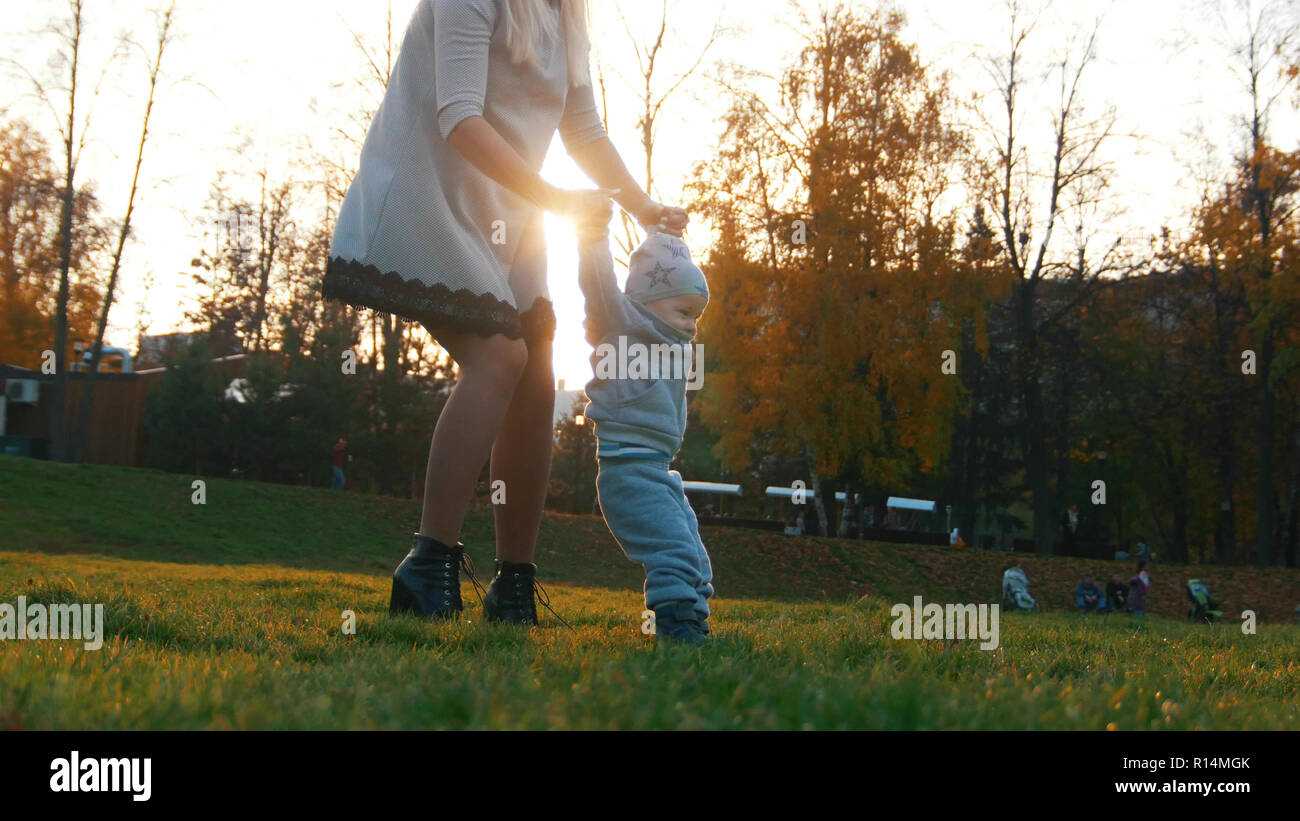Young mother and her little baby teaching how to walk in autumn park ...