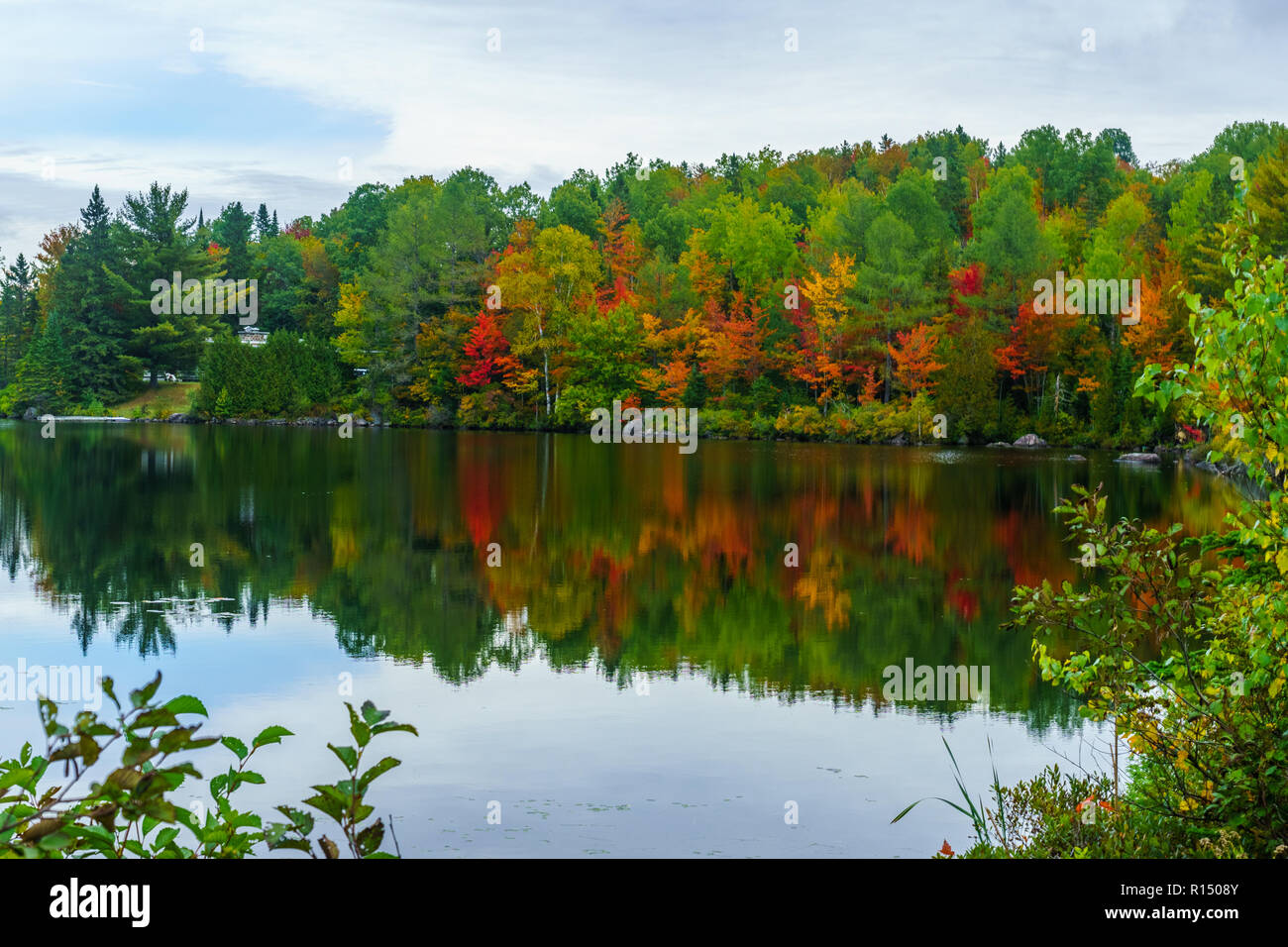 View of Lake Masson, with reflections and fall foliage colors in the Laurentian Mountains, Quebec, Canada Stock Photo