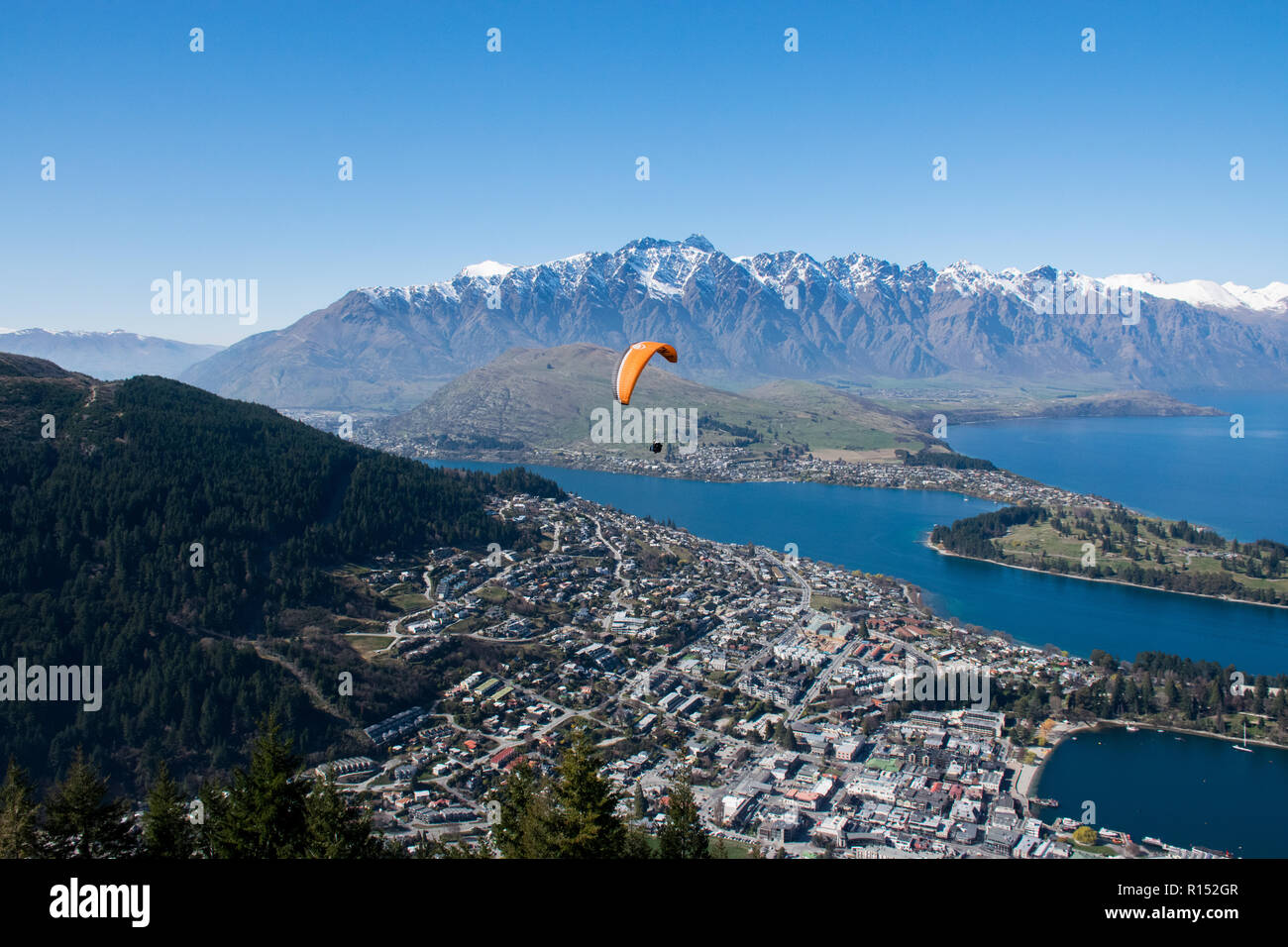 Paraglider flying over Queenstown, New Zealand, with snow capped mountains in the back Stock Photo