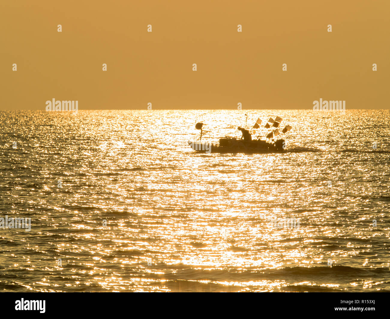 silhouette of a fisherman on small fishing boat on a golden glittering ...