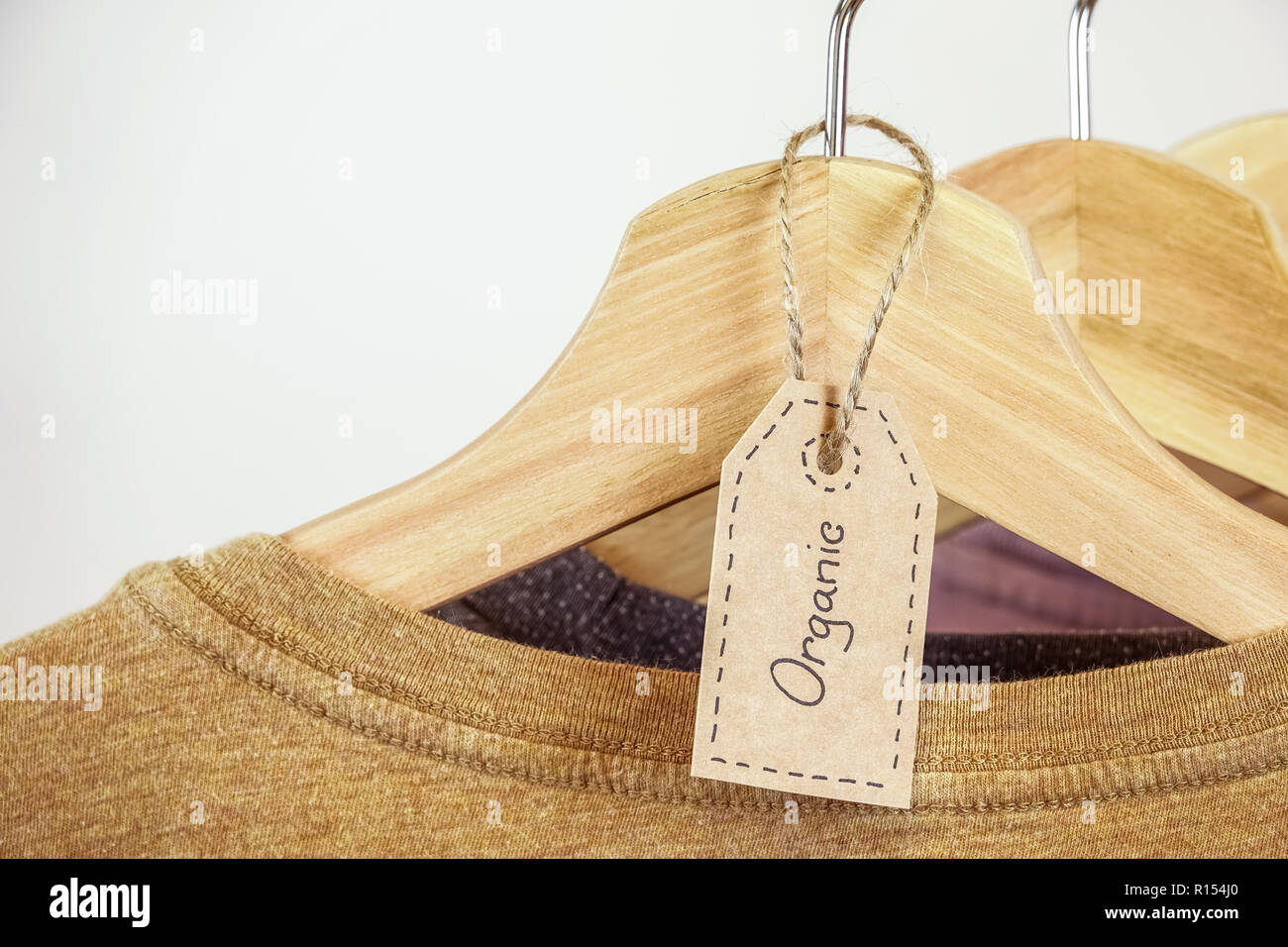 Organic clothes. Natural colored t-shirts hanging on wooden hangers in a row. Stock Photo