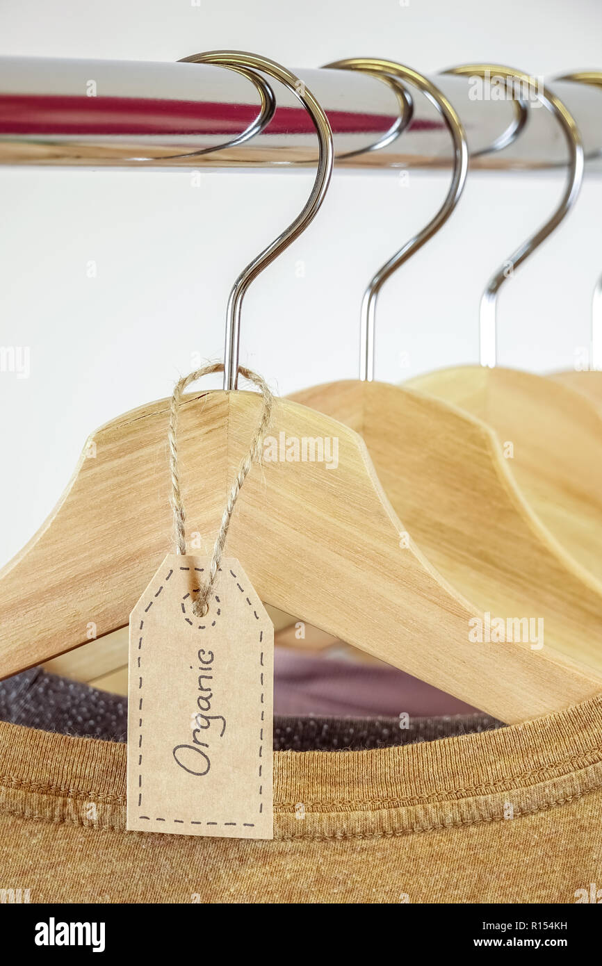 Organic clothes. Natural colored t-shirts hanging on wooden hangers in a row. Stock Photo