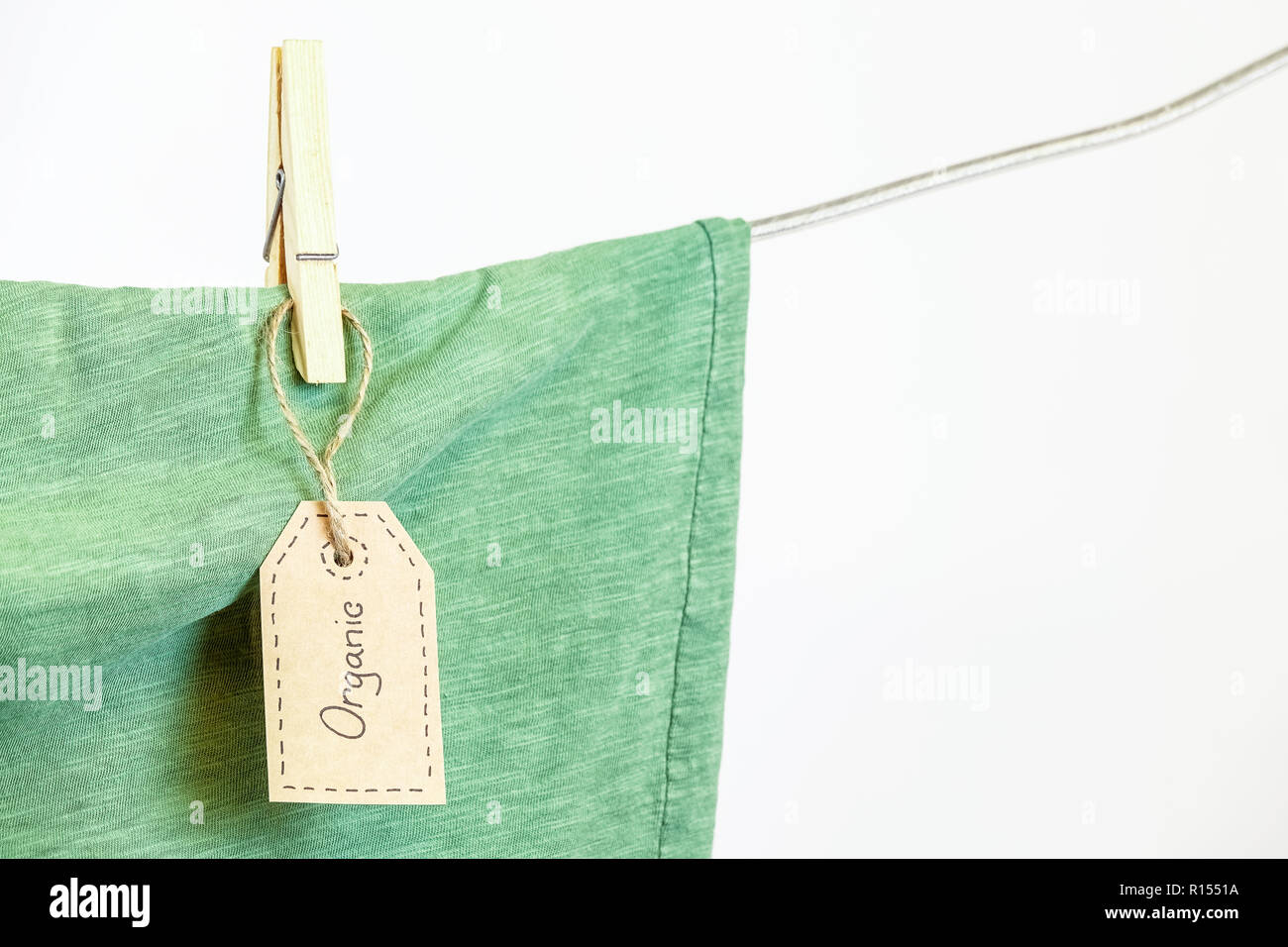 Organic clothes. Green t-shirt hanging on a clothesline. White background. Copy space. Stock Photo