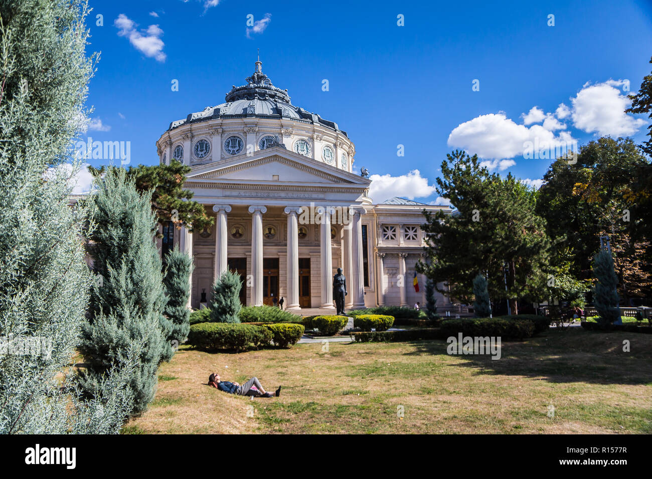 Bucharest, Romania - September 25, 2018 - a woman relaxes in the sun on the grass in front of Roman Athenaeum, Bucharest's most prestigious concert ha Stock Photo