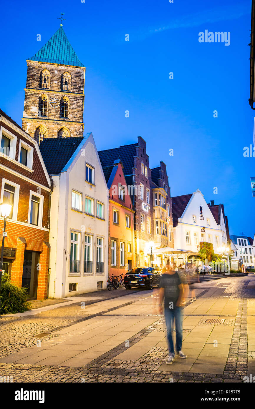 Rheine, Germany - September 5, 2018: man walks down the street in the night, belfry tower of medieval Sankt Antonius Basilica in the backgroung Stock Photo