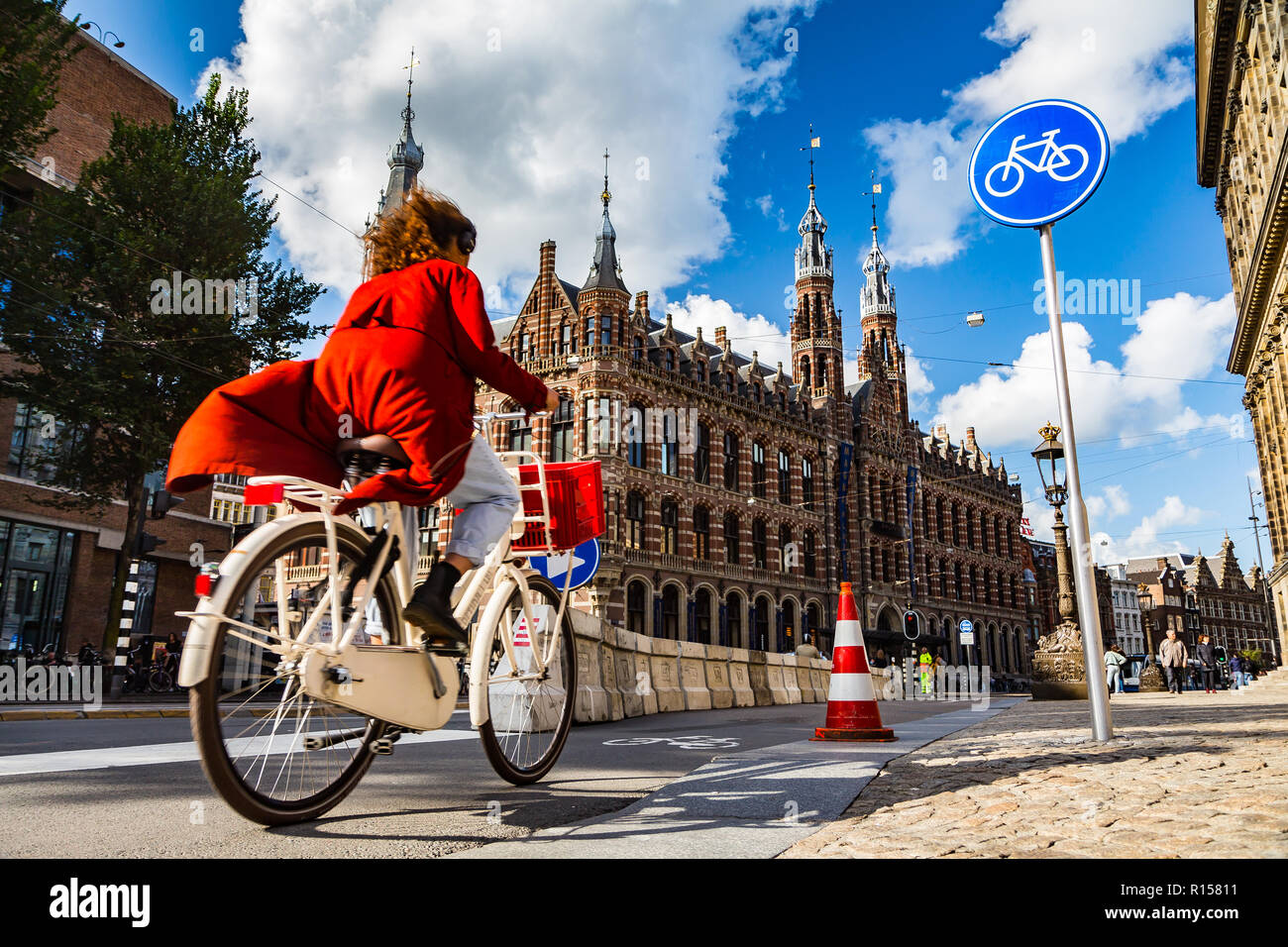 AMSTERDAM, THE NETHERLANDS - September 7, 2018: a woman cycles on Amsterdam street under blue cycle path sign; Magna Plaza shopping mall in the backgr Stock Photo