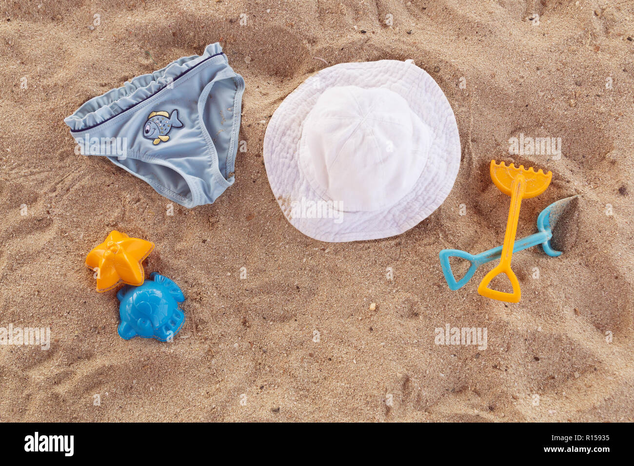 Beach accessories for kids flat lay. Top view of children beach items on sand. Baby plastic scoop, rake, hat and blue children's panties. Water toys. Family summer vacation in tropical resort. Stock Photo