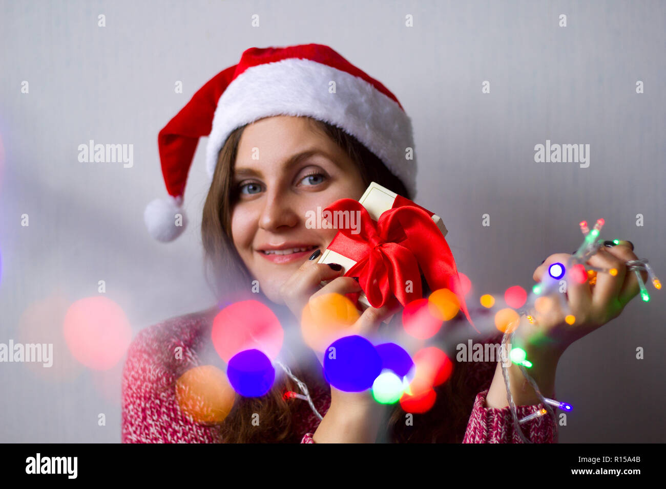 beautiful young woman with shining garland lights  and gift box with red satin ribbon Stock Photo