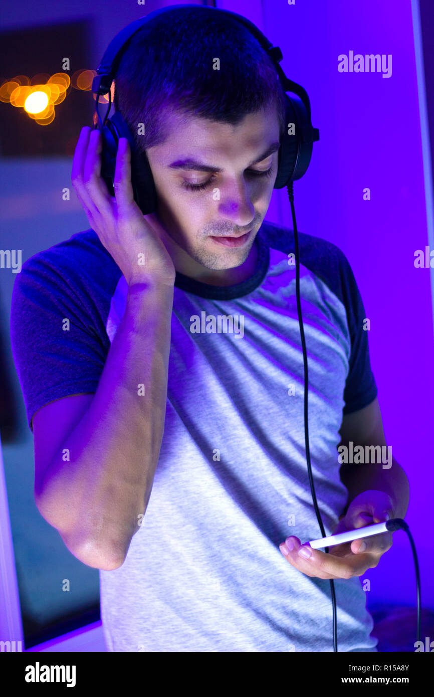 beautiful young cute man with headphones holding a smartphone in his hands and listening to music, neon light, night Stock Photo