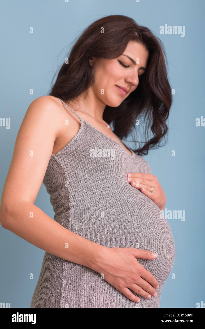 Portrait of happy pregnant woman with hands on belly isolated over blue ...
