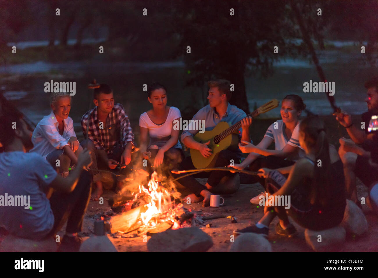 a group of happy young friends relaxing and enjoying summer evening ...