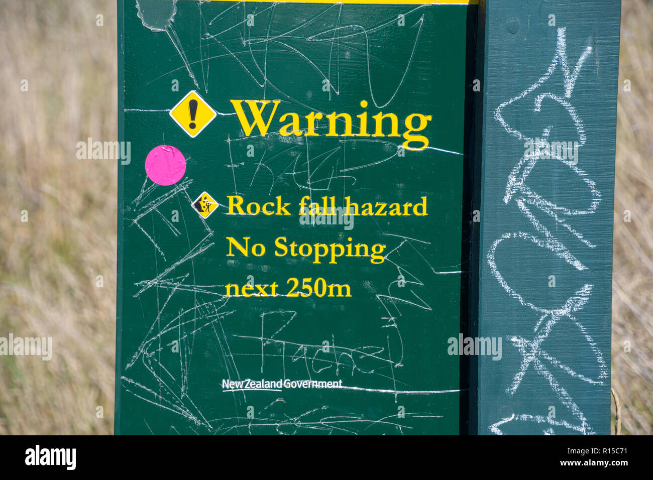 Warning notice of rock fall with graffiti at the coast at Taylors Mistake, Christchurch, New Zealand Stock Photo