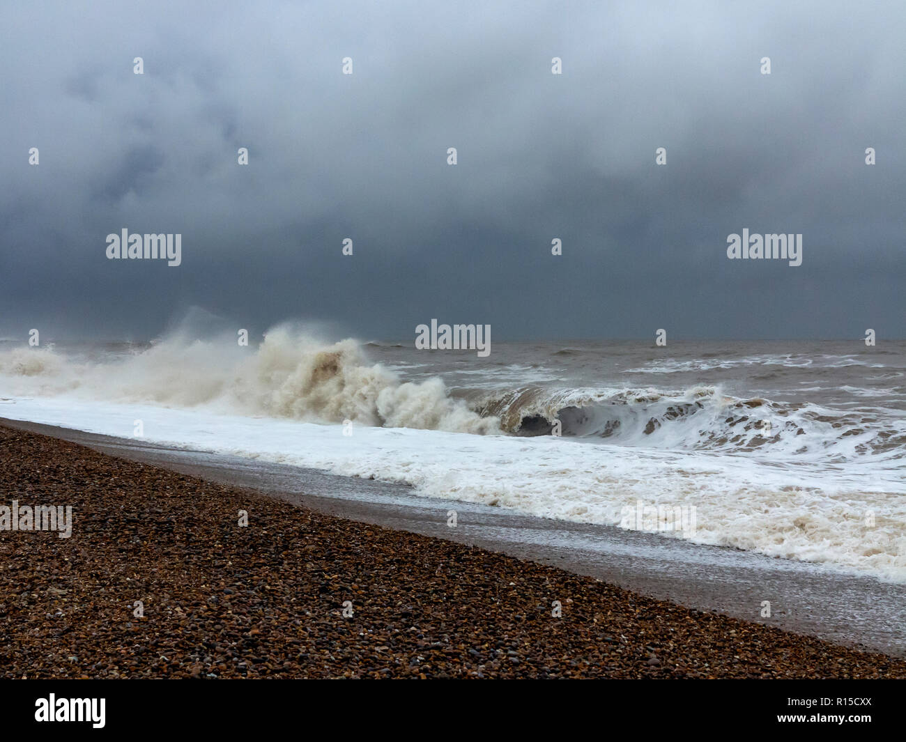 Rough sea breaking on a shingle beach with froth and spray Stock Photo
