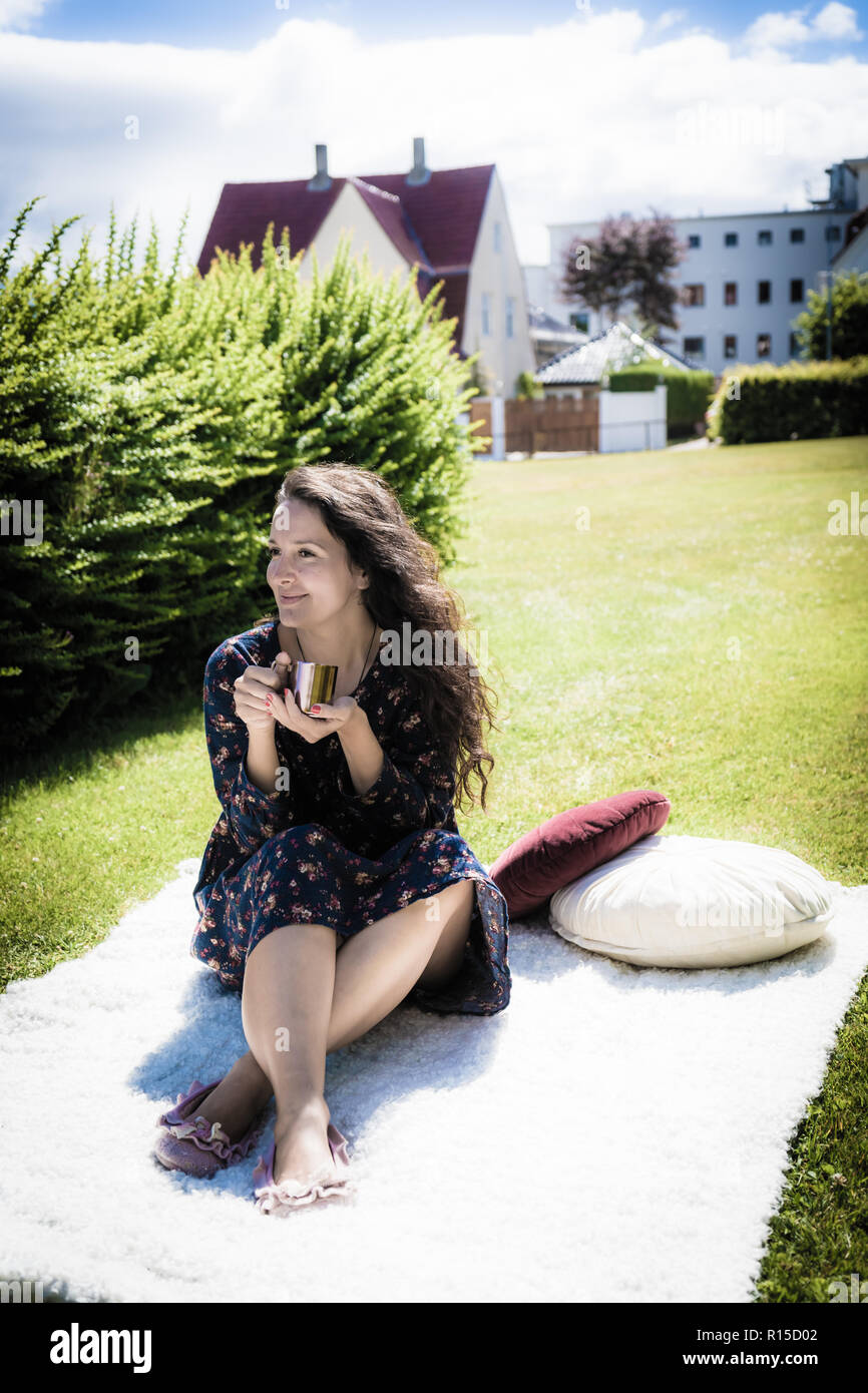 Young pretty woman seating on a cosy blanket in the city park in Scandinavia and having her hot beverage. Stock Photo