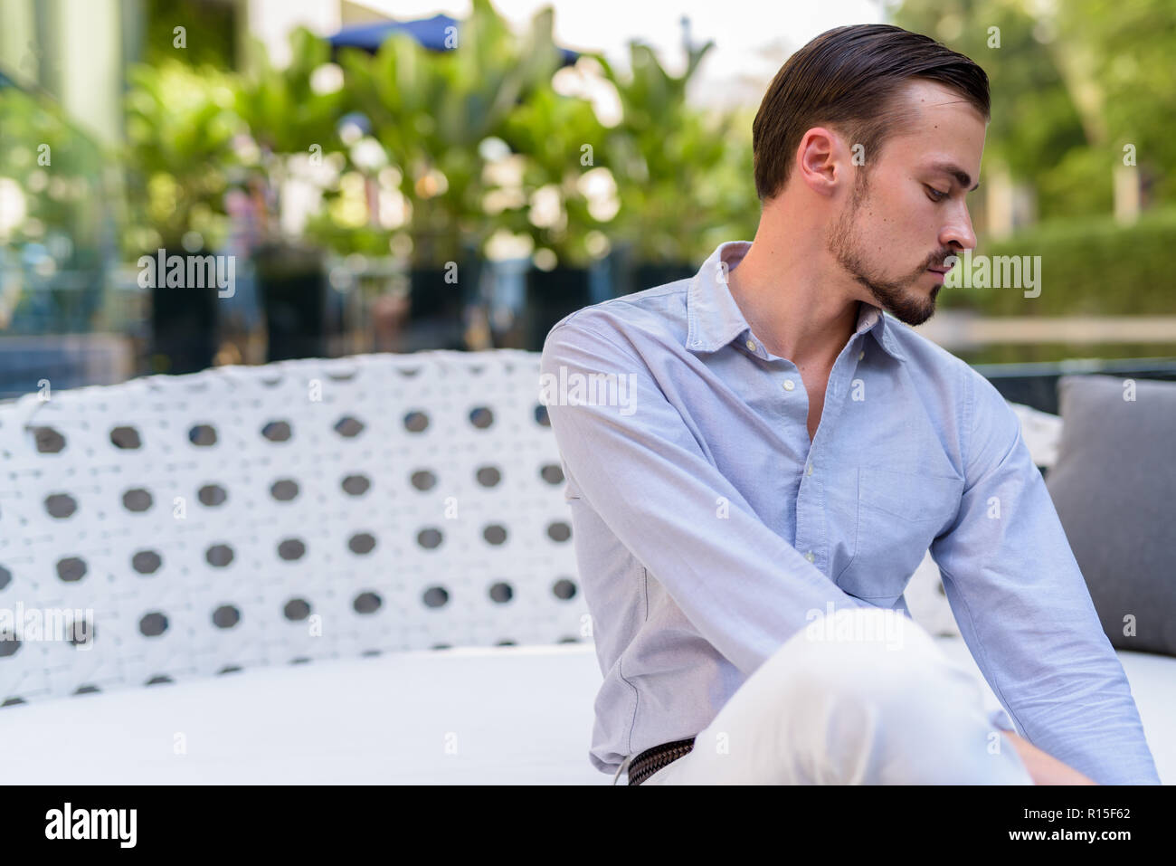 Portrait of young bearded fashionable man sitting outdoors Stock Photo