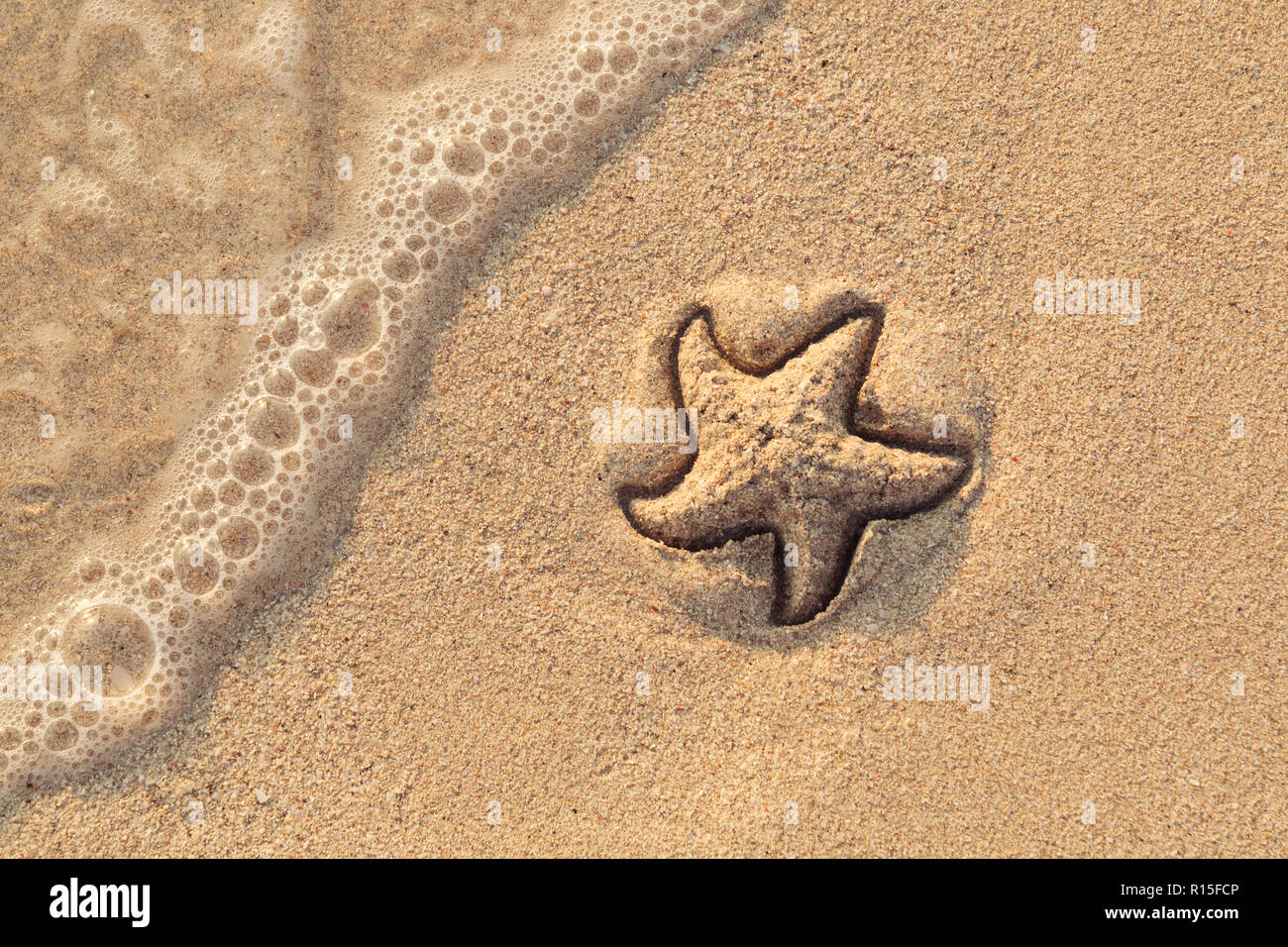 Starfish drawn on the beach sand being washed away by a wave. Foaming sea wave coming to wash a picture on wet yellow beach sand. Holiday and vocation Stock Photo