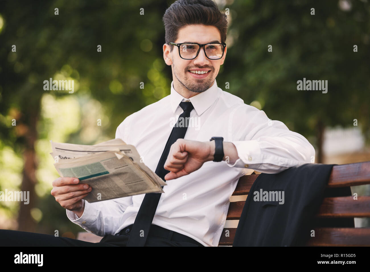 Photo of bearded man in businesslike suit reading newspaper on bench in ...