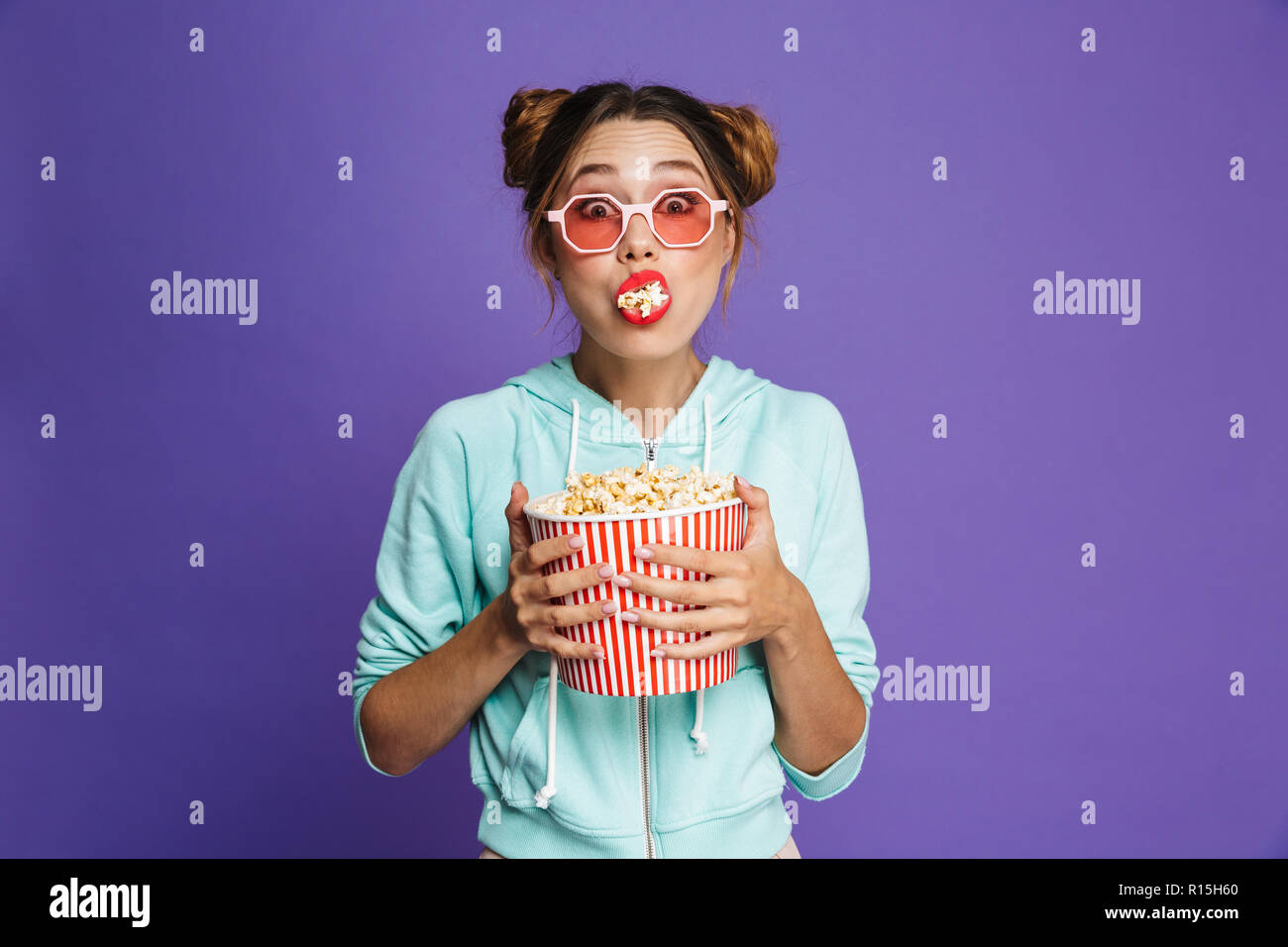 Portrait of a cute young girl with bright makeup isolated over violet background, eating popcorn Stock Photo