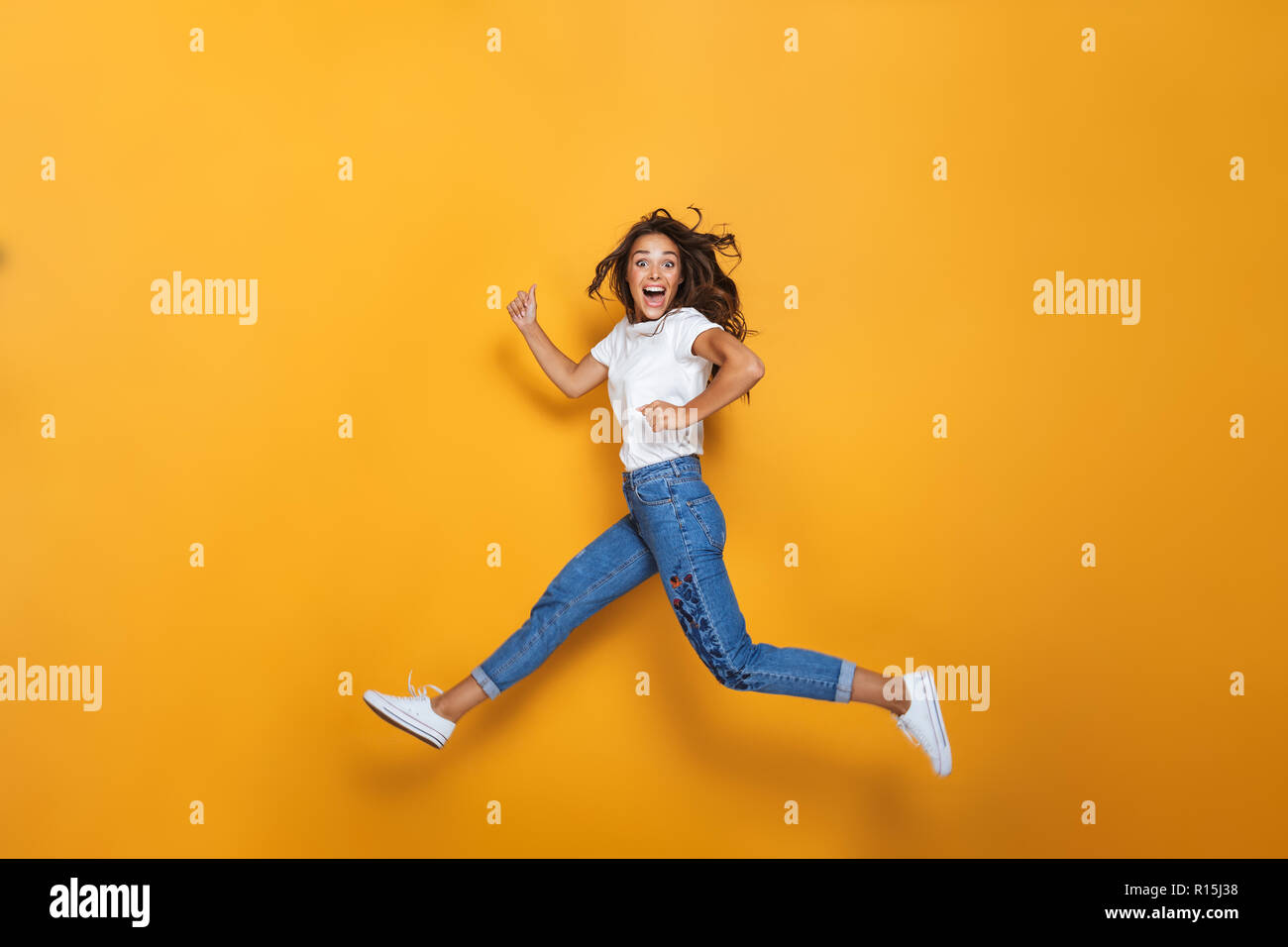 Full length portrait of a happy girl with long dark hair jumping over ...