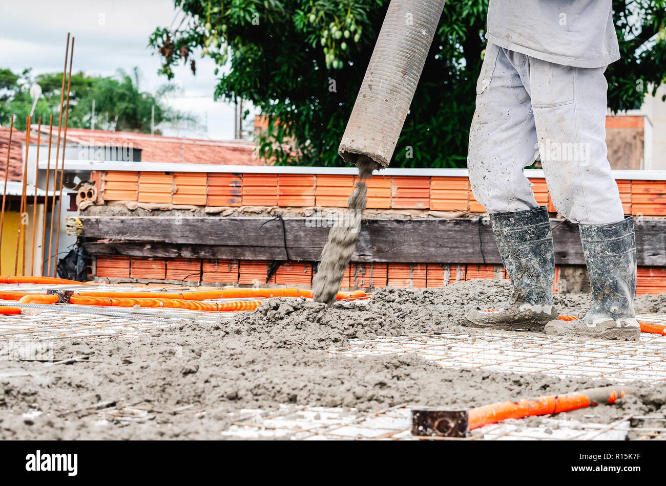 Worker dumping concrete over the slab of a house under construction