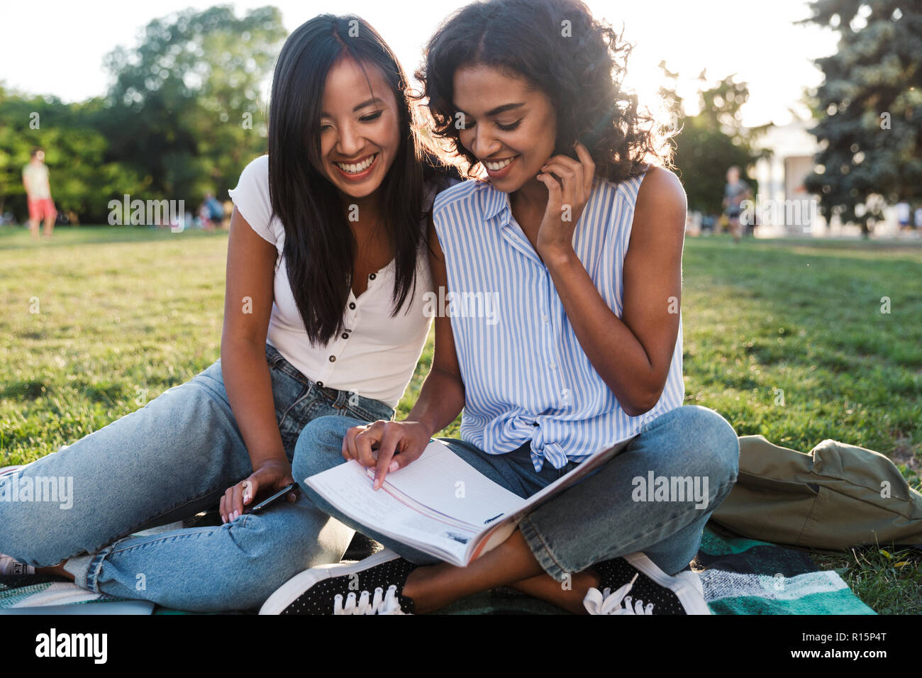 Image of happy smiling young friends girls outdoors in park doing homework. Stock Photo