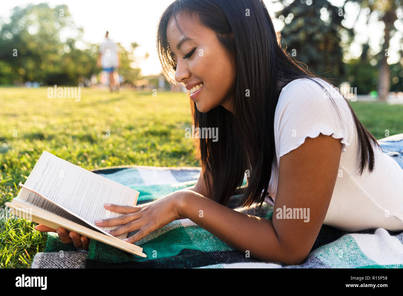 Image of happy smiling young asian girl outdoors in park reading book ...
