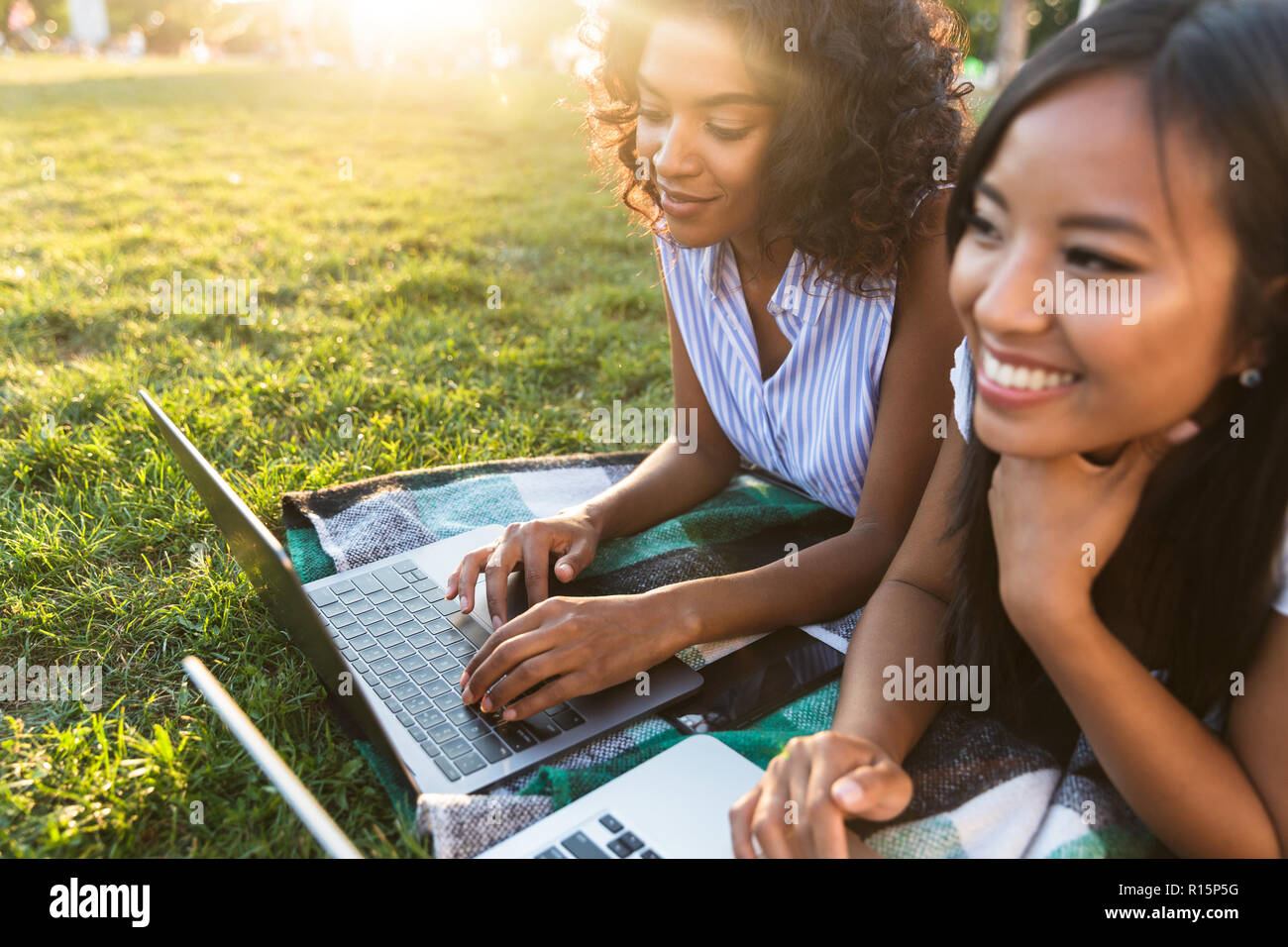 Image of happy smiling young friends girls outdoors in park using laptop computers. Stock Photo