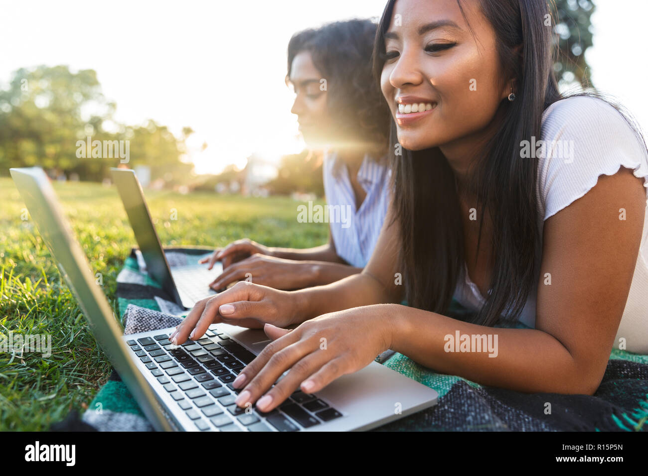 Image of happy smiling young friends girls outdoors in park using laptop computers. Stock Photo