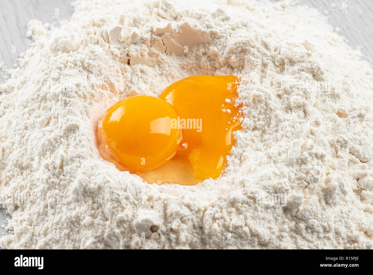 pile of flour with egg yolks for dough on table Stock Photo
