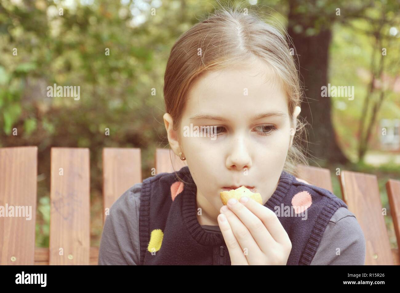 Caucasian 8 years old child, girl, sitting on a bench and eating a biscuit in the park Stock Photo