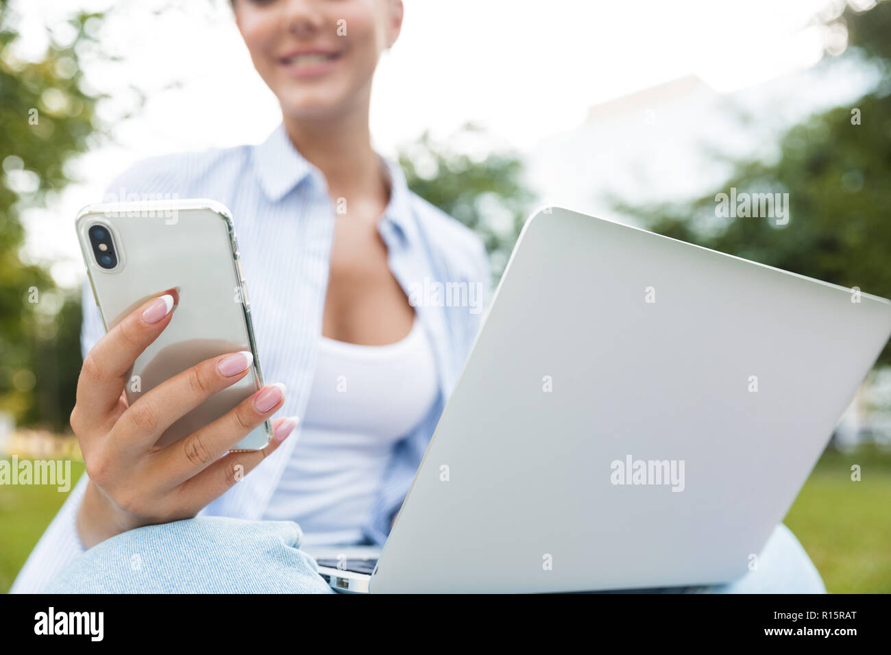 Cropped photo of young woman in park outdoors using laptop computer and mobile phone. Stock Photo
