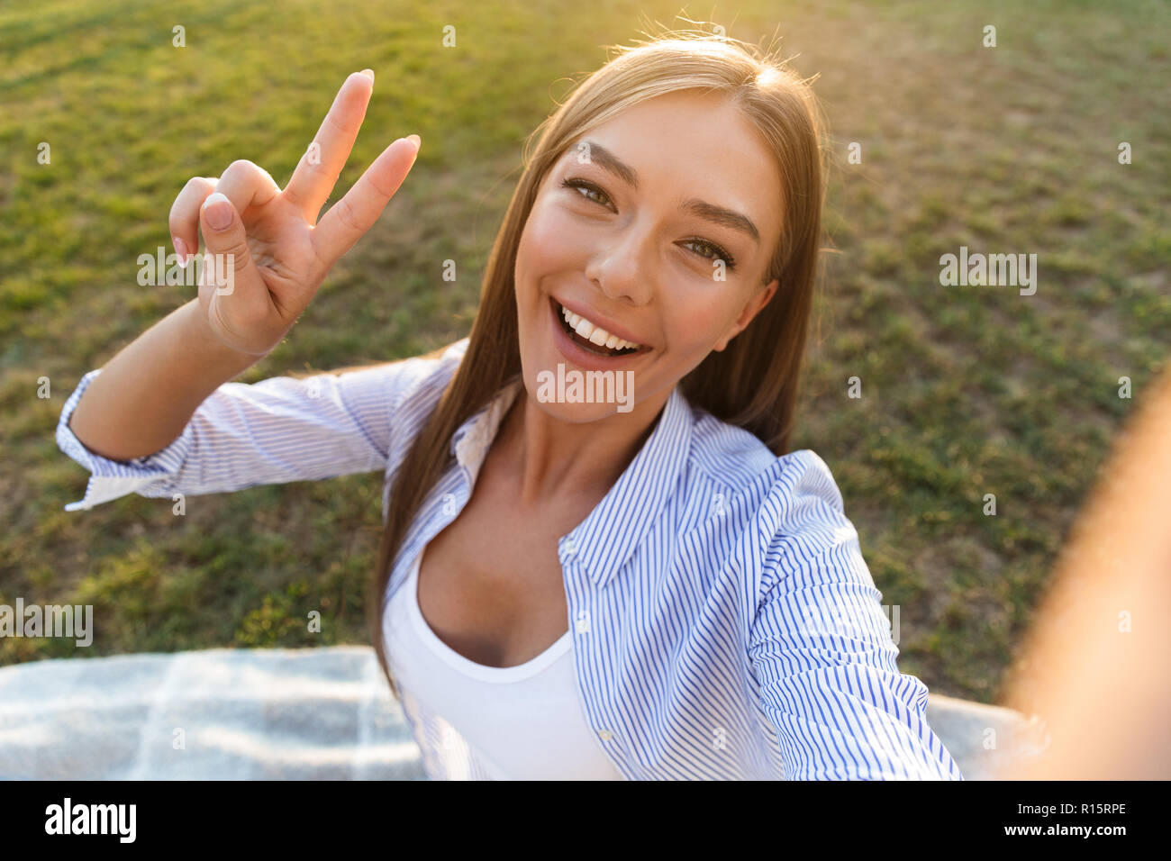Close up of a cheerful young woman taking a selfie at the park with outstretched hand Stock Photo