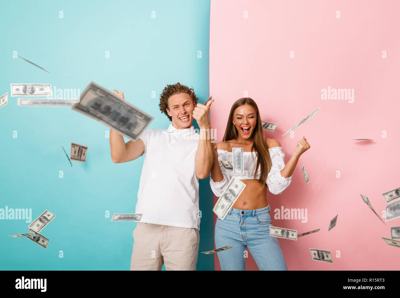 Portrait of a happy young couple standing over two colored background, standing under money banknotes shower Stock Photo