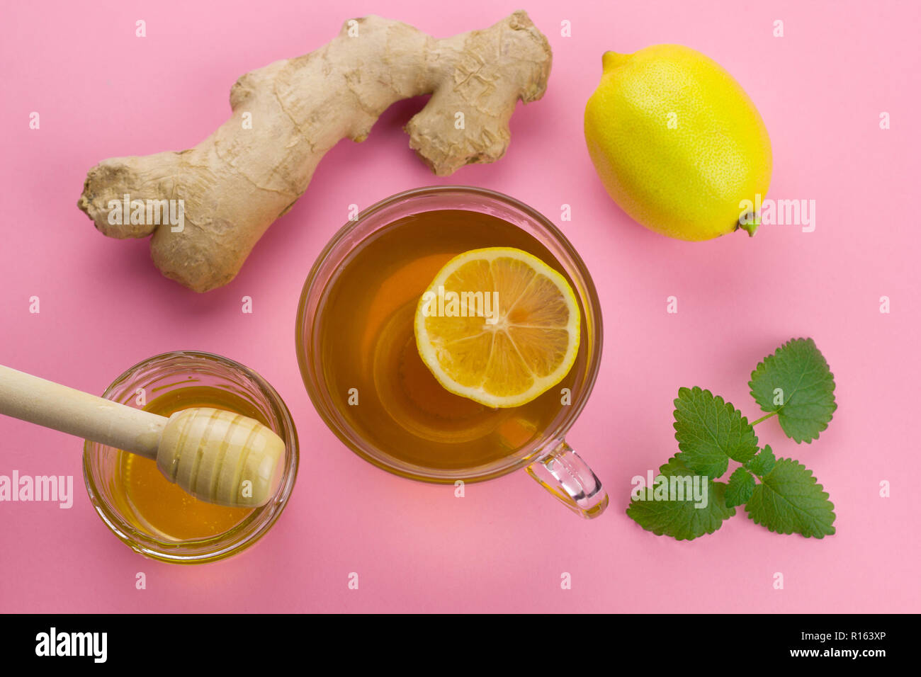 top view tea,  lemon,ginger, mint   and liquid honey jar with wooden spoon on a pink vibrant background healthy anti cold drink alternative medicine Stock Photo