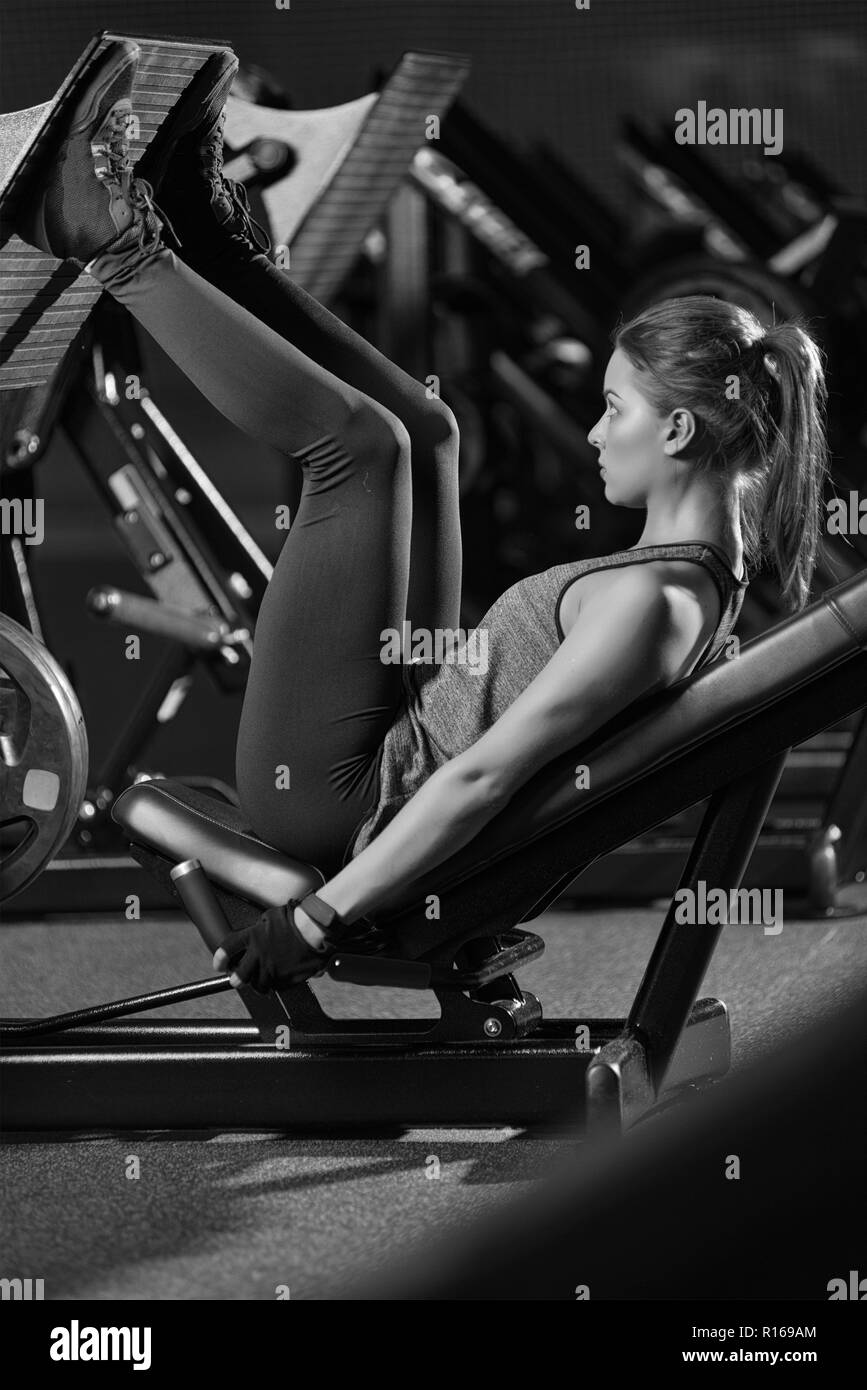 Sportive woman using weights press machine for legs. Gym. Stock Photo