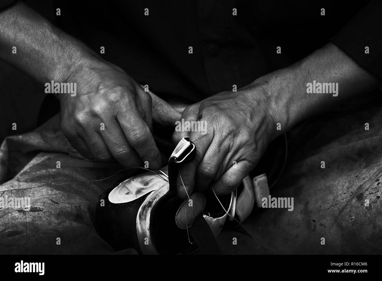 A man who repairing a shoe at the side of street on Tehran, capital of Iran. the black and white photo with contrast of a shoe maker with strong hand. Stock Photo