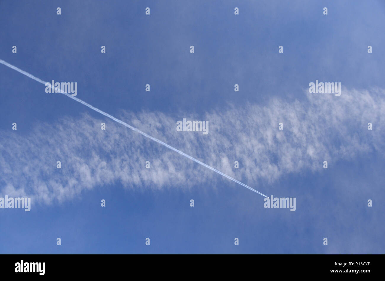 An airplane draws a contrail that crosses an elder and diffused contrail. Stock Photo