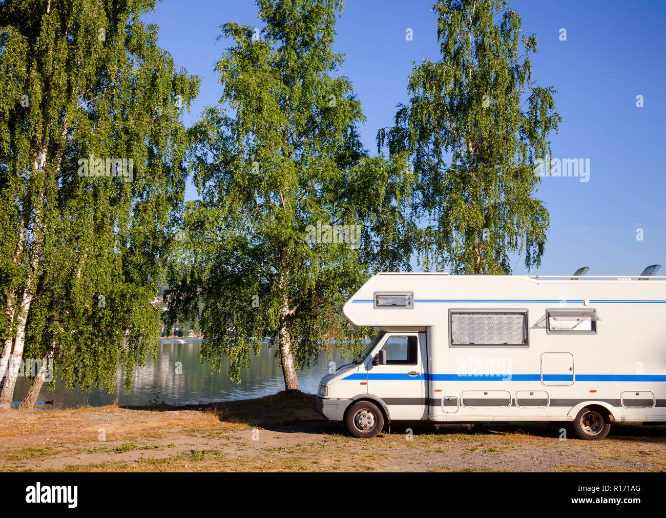 Camper van recreational vehicle (RV) parked at campsite on a lake shore by the birch trees in Southern Norway - norwegian summer travel concept Stock Photo