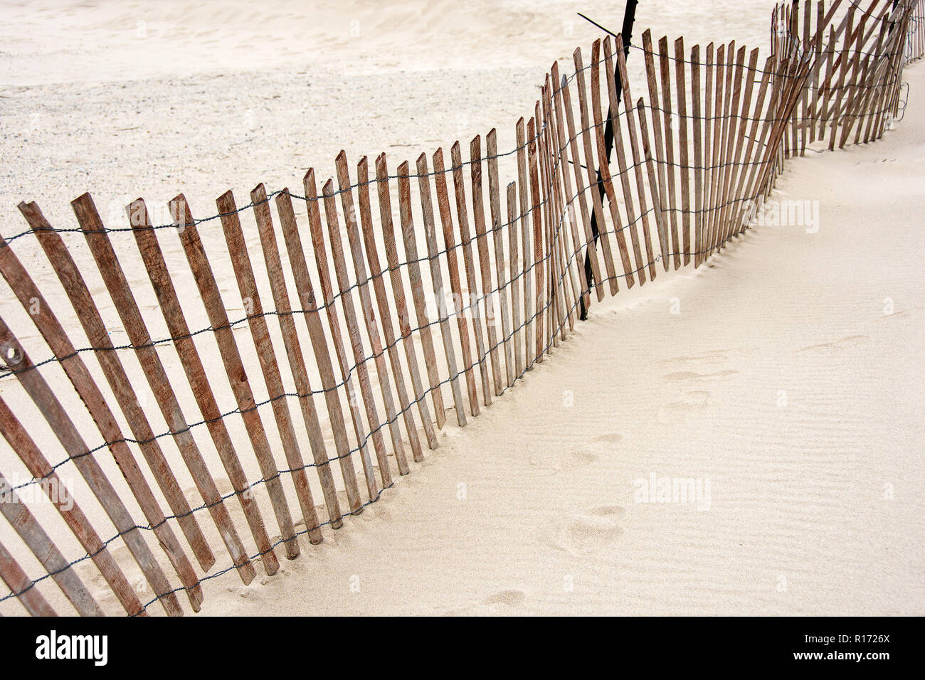 slanted weathered old wooden fence in sand on vacant beach Stock Photo