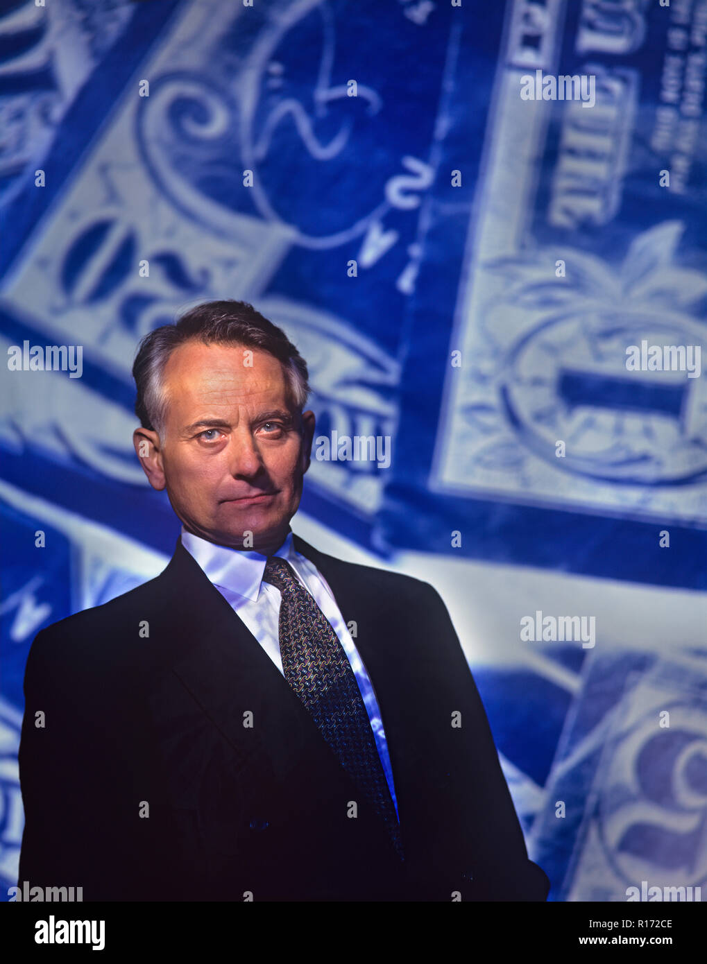 Mature businessman or banker standing in front of a paper currency background with symbolism of greed, corruption and deceit on his face Stock Photo