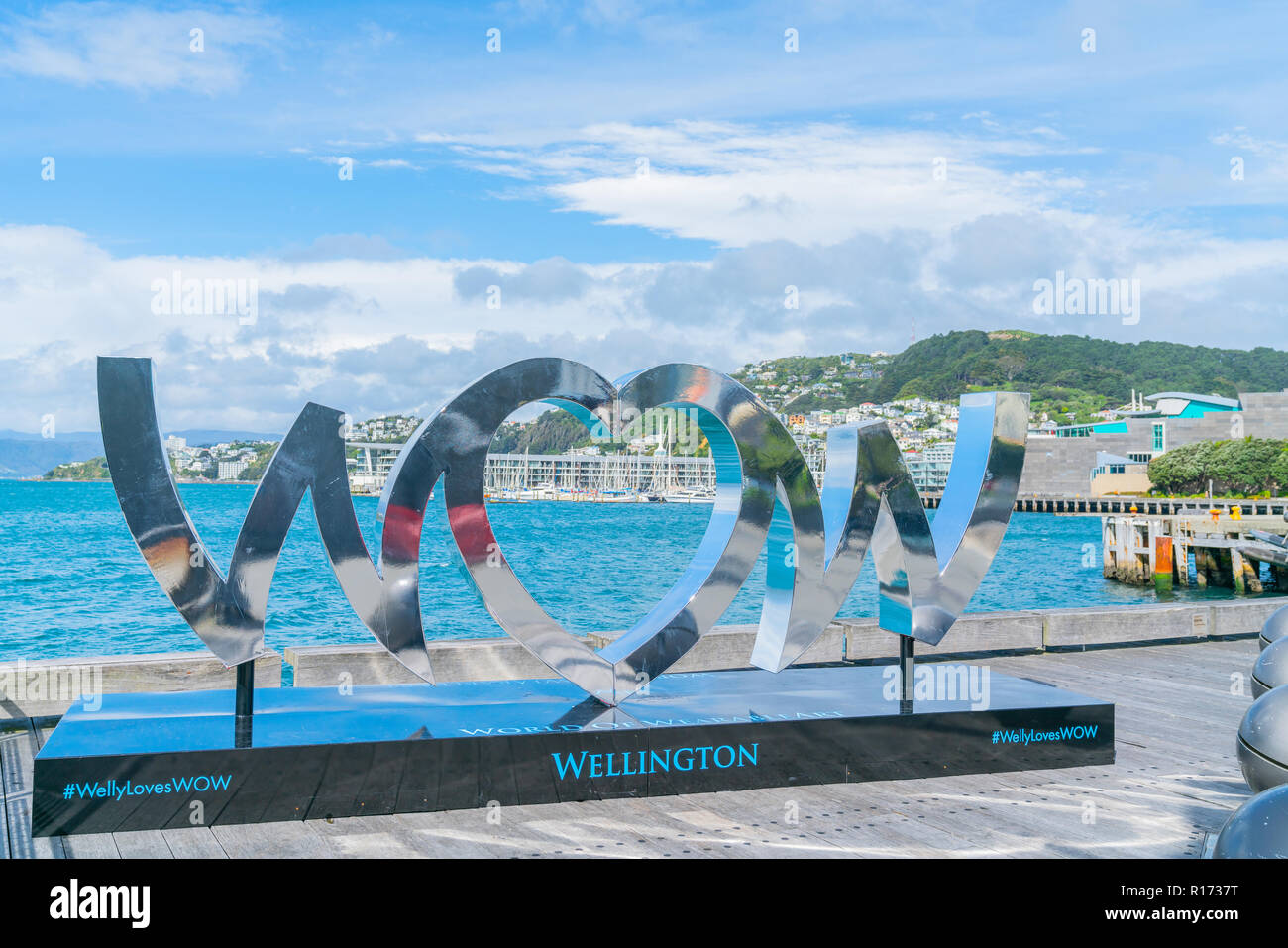 WELLINGTON, NEW ZEALAND - OCTOBER 1 2018; World of Wearable Art iconic shiny silver WOW sign on city waterfront reflects city and arbour scenes and hi Stock Photo