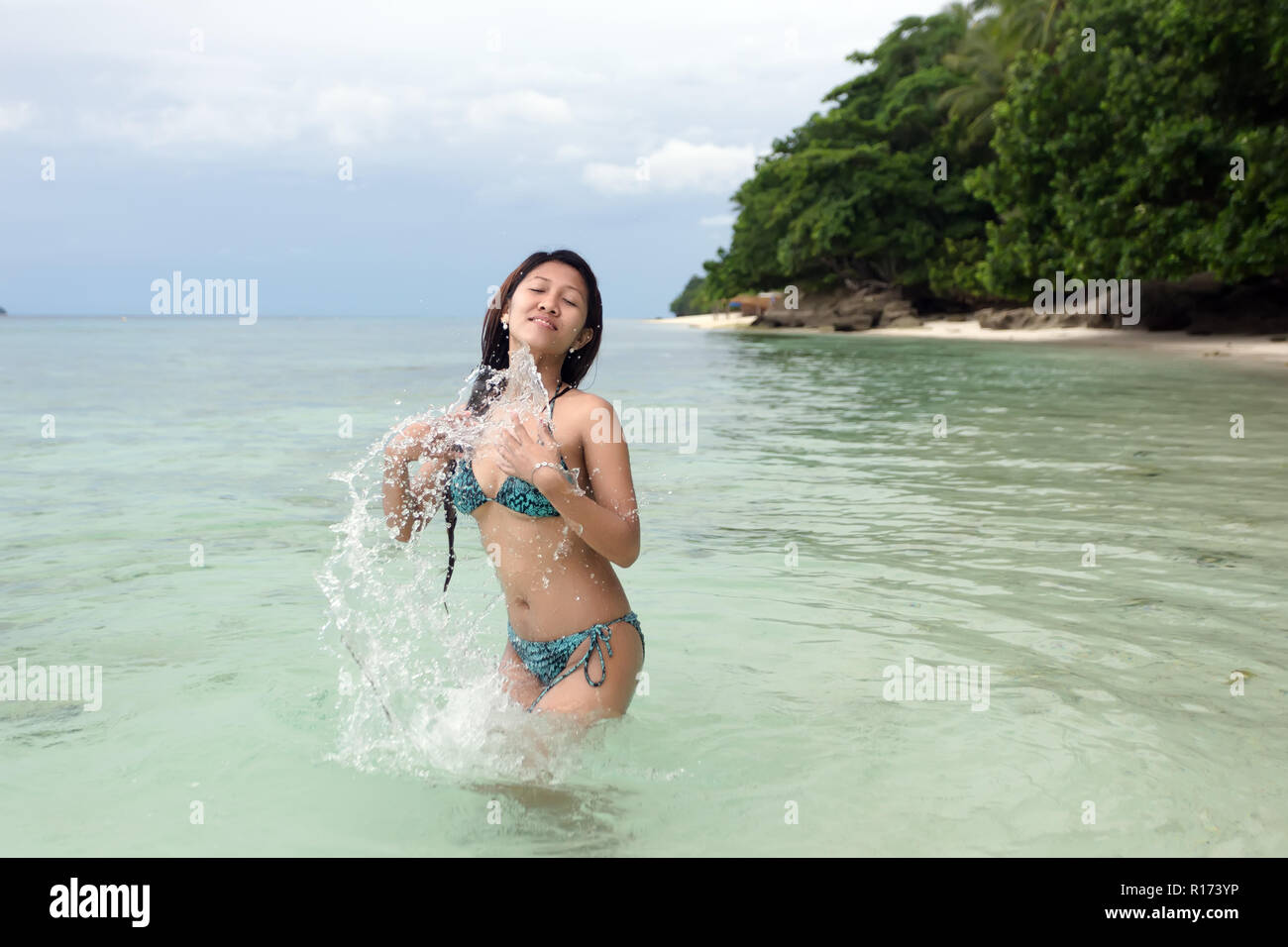 Happy carefree Asian woman in a bikini playing in the sea splashing herself  with water as she enjoys cooling off in the hot summer sunshine Stock Photo  - Alamy